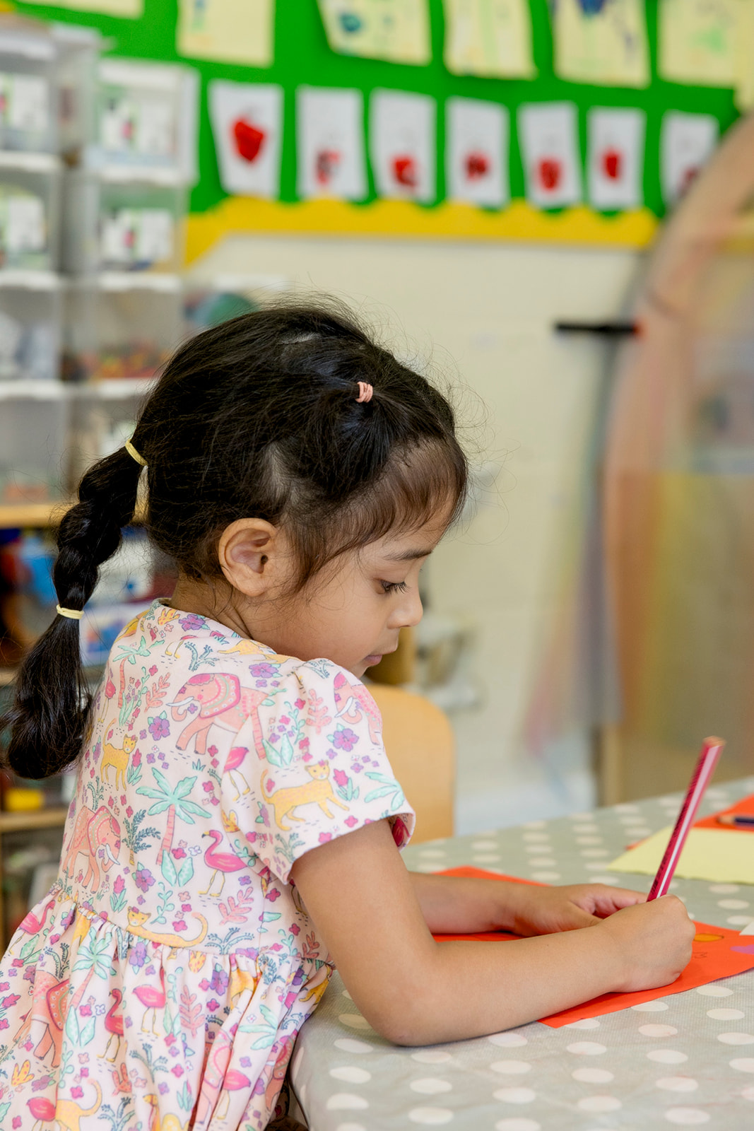 A girl concentrating on a drawing at the art table with a pot of pencils beside her