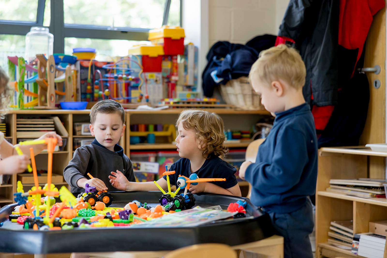 Three boys building with colourful construction toys at a black tuff tray in the preschool room